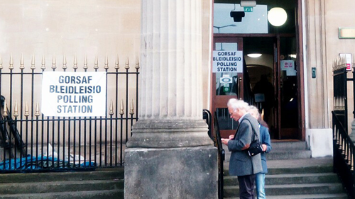 Older gentleman and lady standing by a pillar outside a polling station